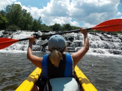 Woman in whitewater raft holding oar above her head.
